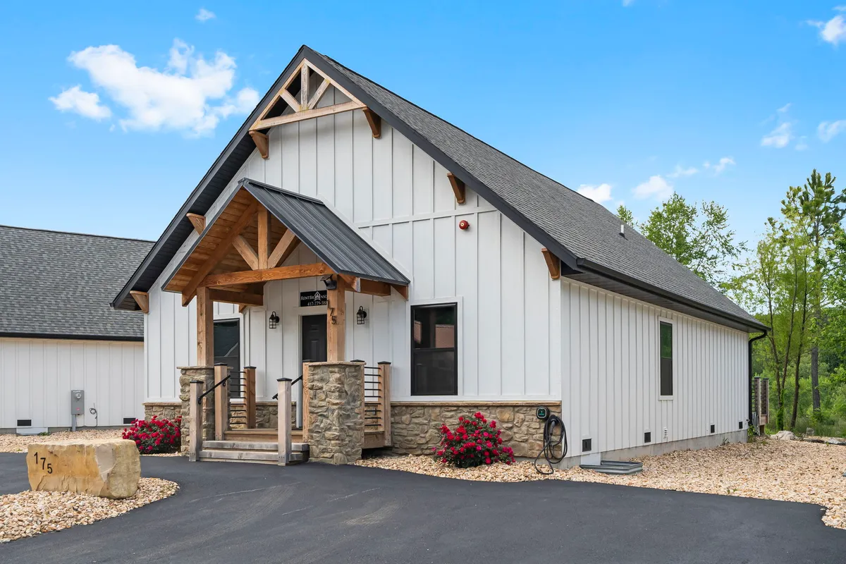 A welcoming front porch with wooden beams, stone accents, and colorful flower beds, creating an inviting entrance to the property. The scene suggests a place where guests gather, relax, and enjoy the outdoors, with comfortable seating perfect for morning coffee or evening sunsets.