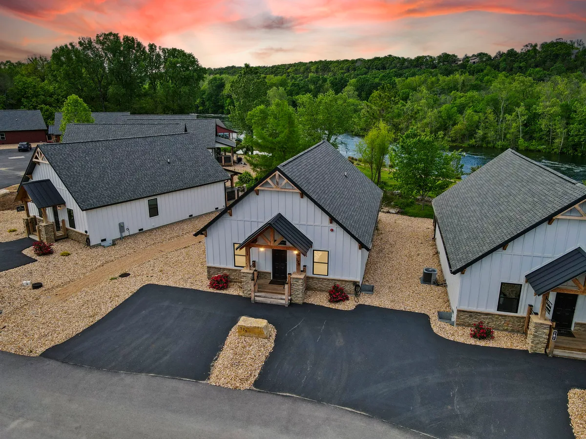 This exterior image features modern cabins nestled along a landscaped garden with a scenic river view, all set beneath a colorful sunset sky. The setting exudes tranquility while suggesting a gathering-friendly atmosphere ideal for families.
