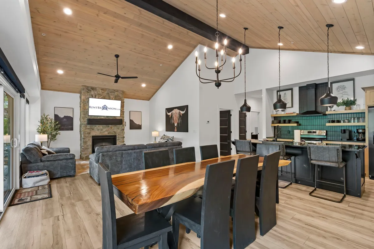 An open-concept space that includes a large dining table, a stone fireplace, an open kitchen area, and comfortable seating. The layout is designed to foster togetherness, with transitions between spaces for dining, relaxing, and entertaining.